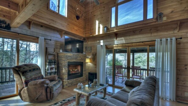 A log cabin interior with a fireplace, a sofa, a recliner, and a glass coffee table. - RIVER, HOT TUB, GAME ROOM, PETS - 4 Pool, Playground, Dog Park, Arcade, Tennis. (Ellijay)