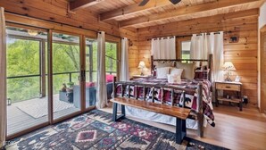 A wooden cabin bedroom with a large bed, a bench, a ceiling fan, and a view through the glass doors. - RIVER, HOT TUB, GAME ROOM, PETS - 4 Pool, Playground, Dog Park, Arcade, Tennis. (Ellijay)