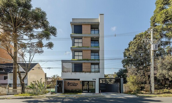 A multi-story building with a modern design, featuring balconies with greenery, a visible entrance, and a sign indicating it is a hotel. - Your Complete Stay in a Building w/ a gym and Garage in Curitiba - Plags (Curitiba)