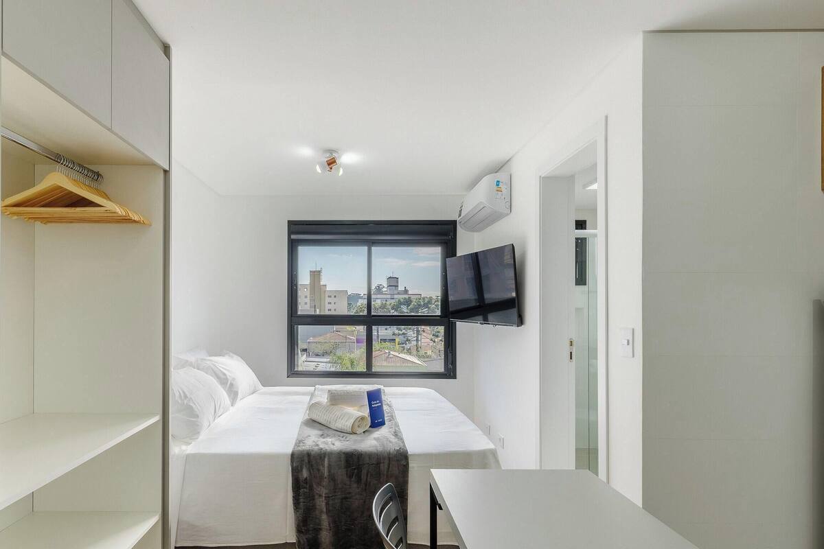 Habitación de hotel moderna y minimalista con una cama grande, un televisor montado en la pared y una ventana con vistas a la ciudad.