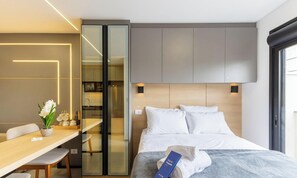 A modern hotel room with a bed, bedside table, and a desk area with chairs. - Your Complete Stay in a Building w/ a gym and Garage in Curitiba - Plags (Curitiba)