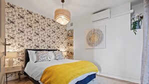 Un dormitorio con cama, mesita de noche, lámpara, pared con papel tapiz floral e iluminación en el techo.
