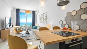 Una sala de estar moderna con una mesa de comedor de madera, sillas amarillas y vista al mar a través de amplios ventanales.