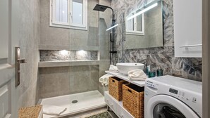 Un baño moderno con ducha de vidrio, lavabo integrado y lavadora.
