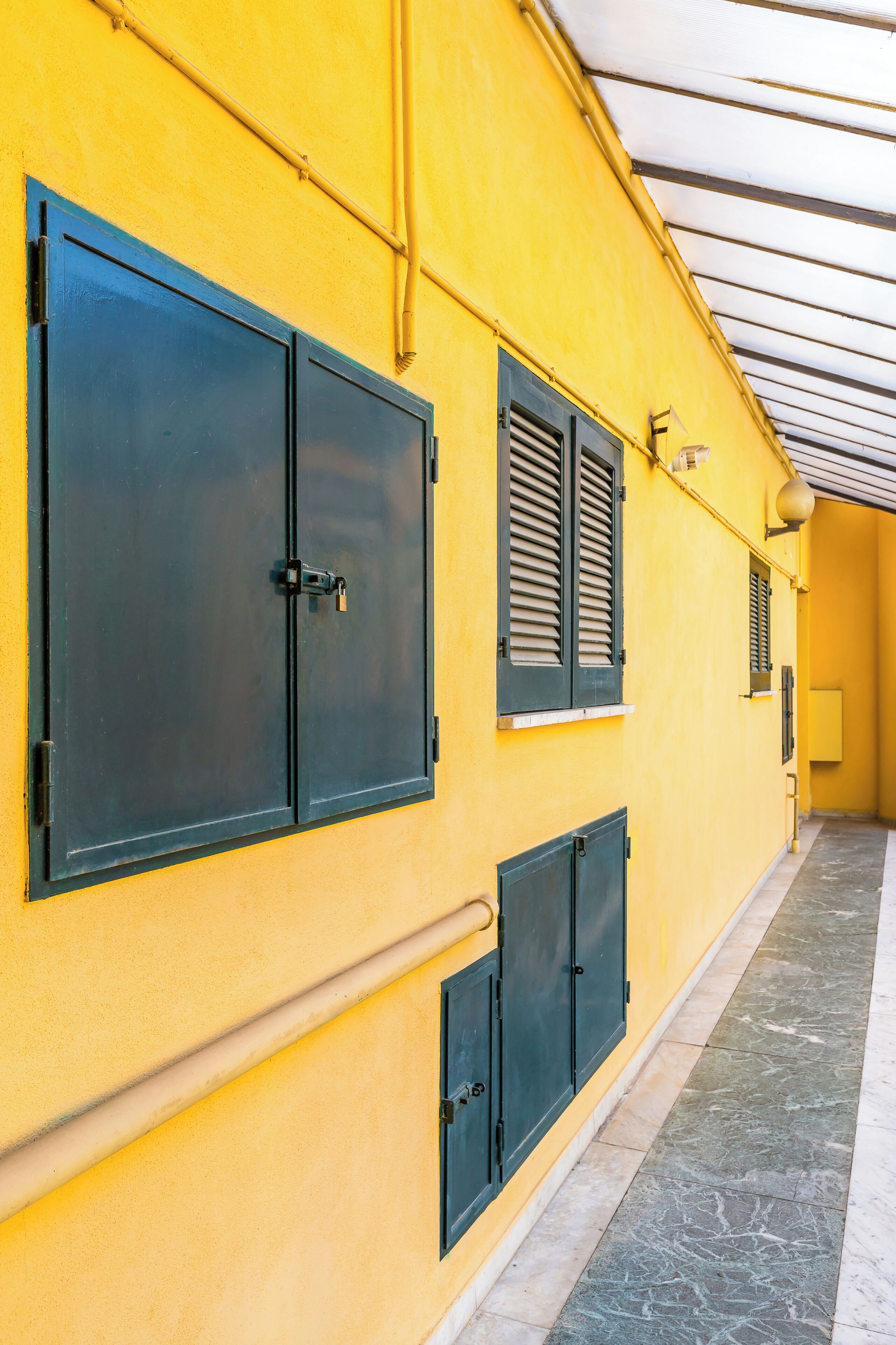 A corridor with yellow walls, black shutters, and a tiled floor.