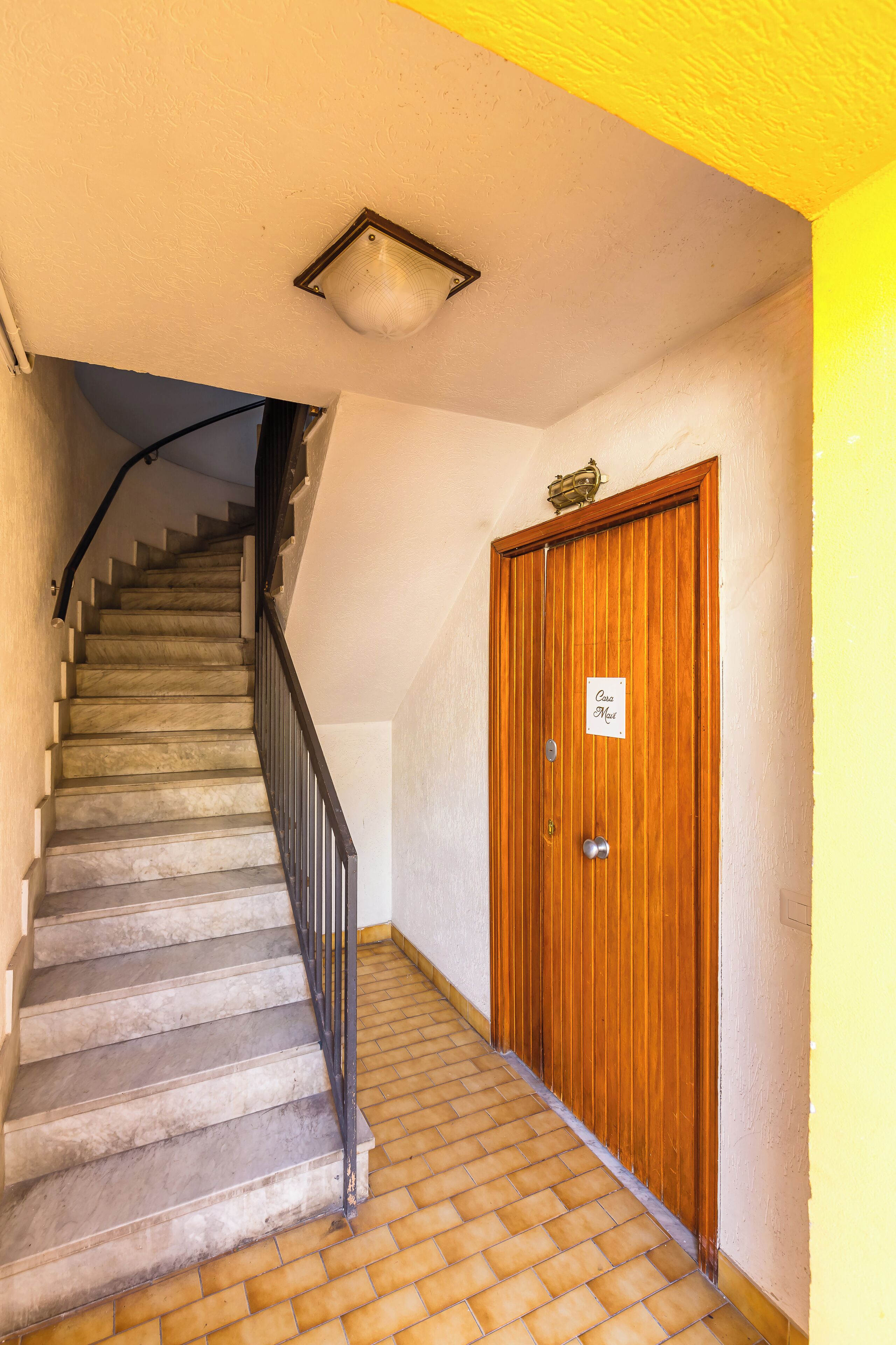 Uma escadaria leva a uma porta de madeira com uma placa que diz 'Casa Meet'.