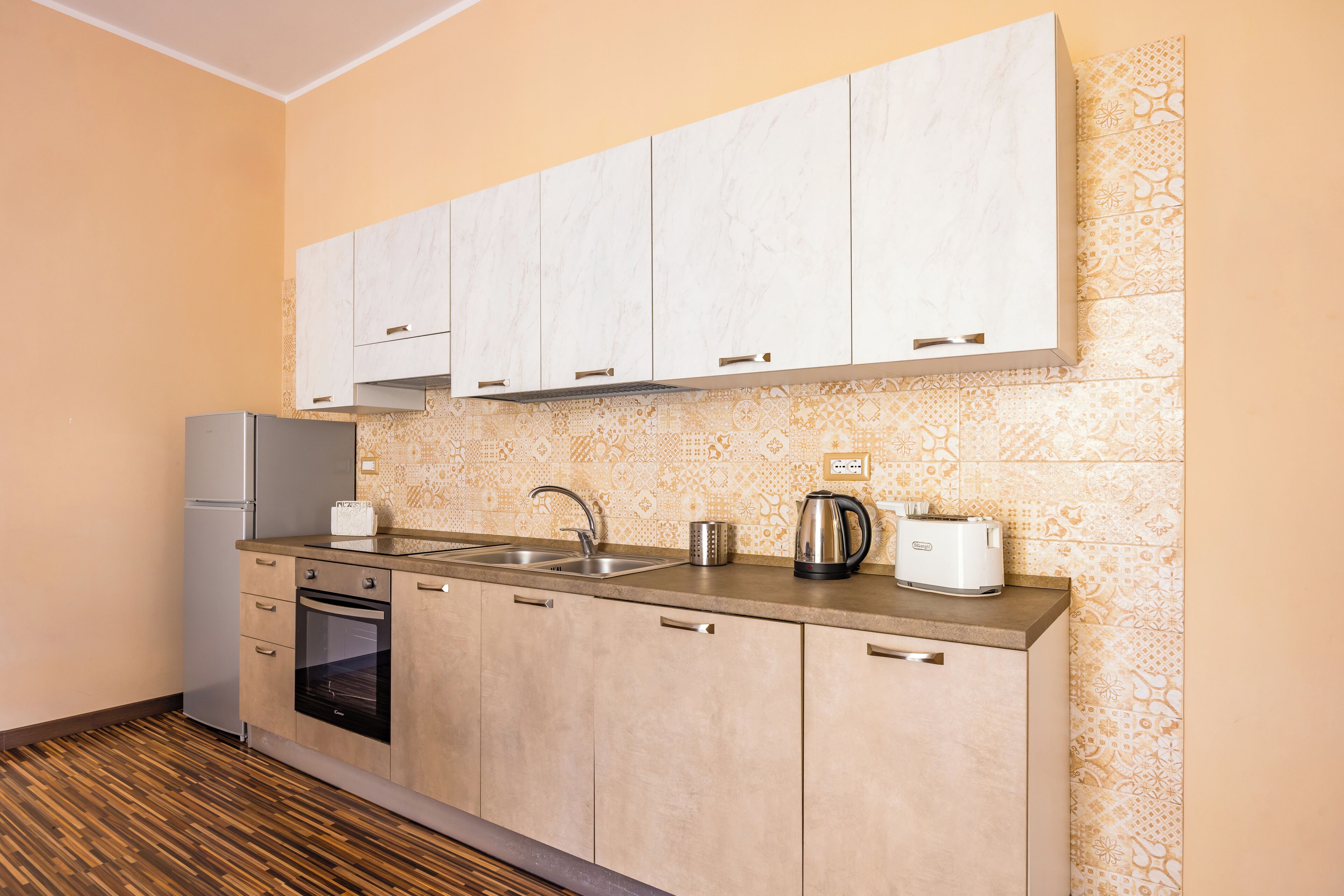 Una cocina compacta con horno integrado, un refrigerador de acero inoxidable, un lavamanos doble y una tetera.