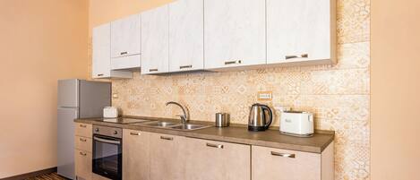 A compact kitchen with a built-in oven, a stainless steel refrigerator, a double sink, and a kettle.