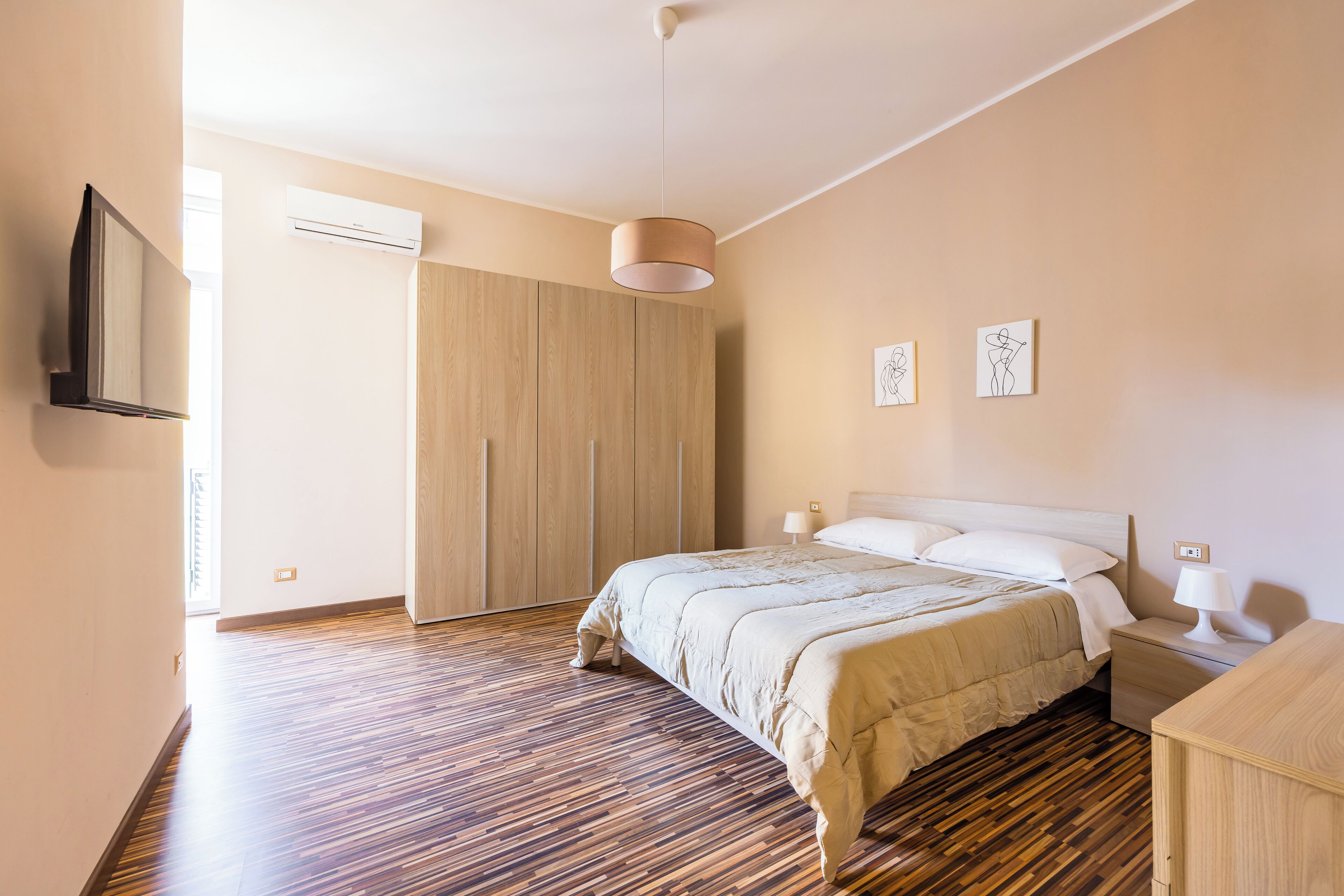 A bedroom with a bed, bedside lamps, a wardrobe, and artwork on the wall.