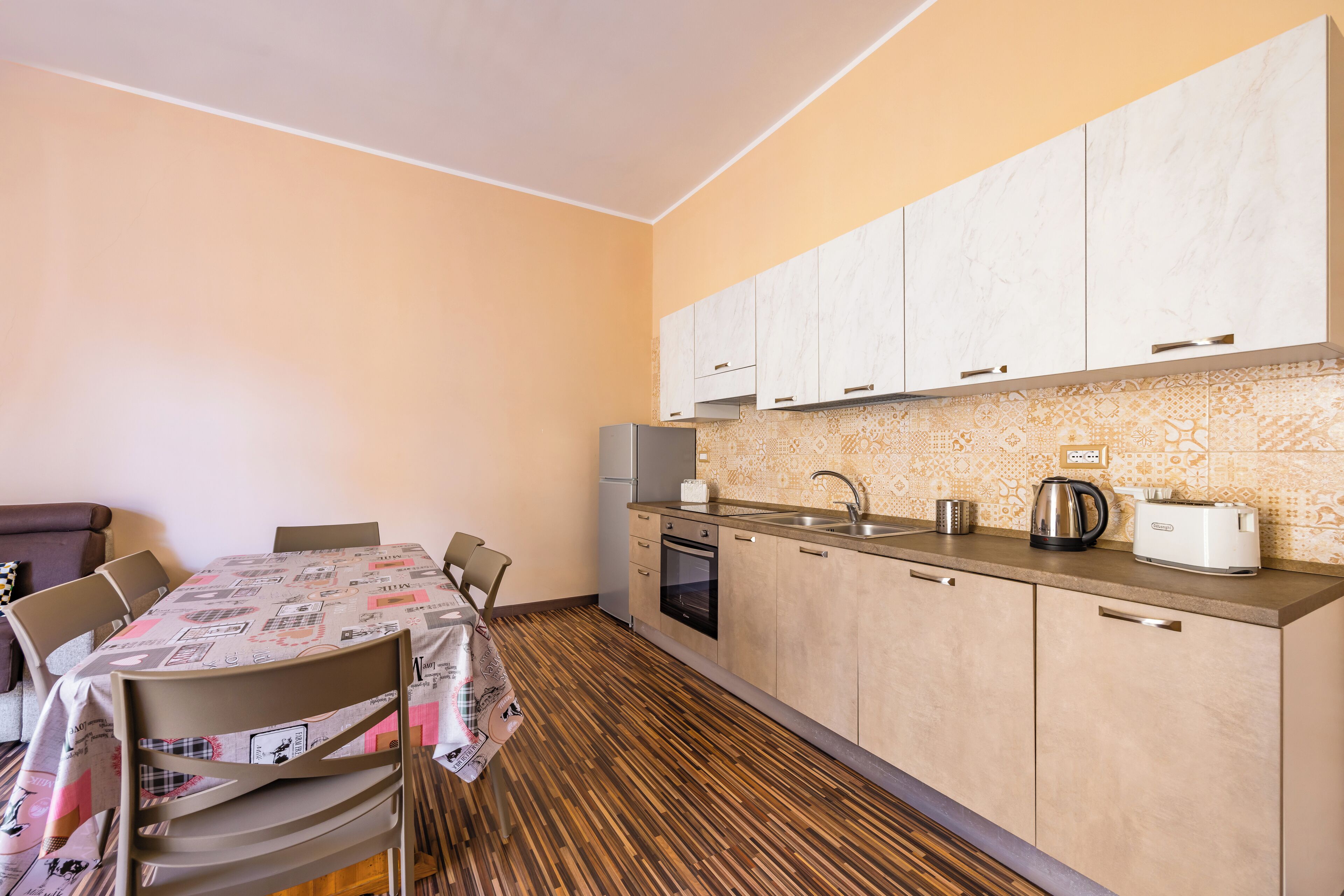 Una cocina compacta con zona de comedor, que presenta piso de madera, horno integrado y pileta con hervidor y tostadora.