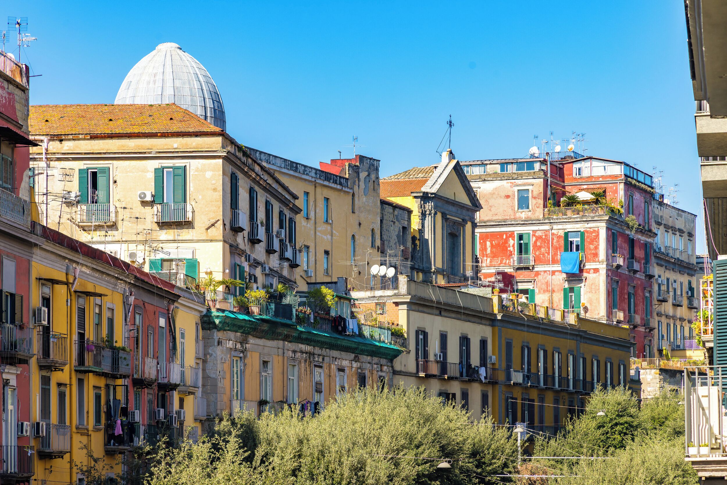 A row of colorful buildings with balconies, a dome structure, and a clear blue sky.