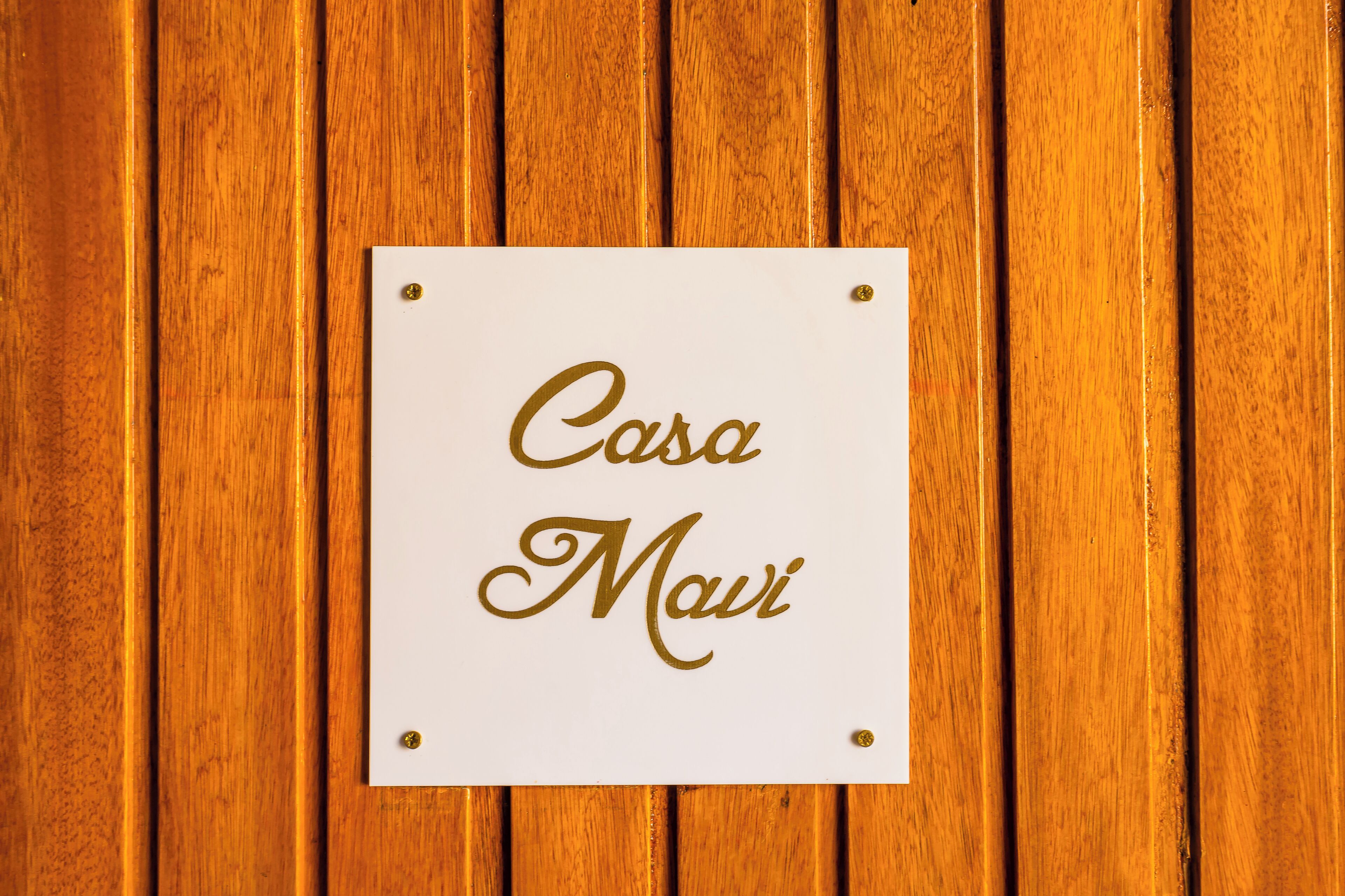 Een bord met de tekst 'Casa Mai' op een witte achtergrond, bevestigd aan een houten muur.