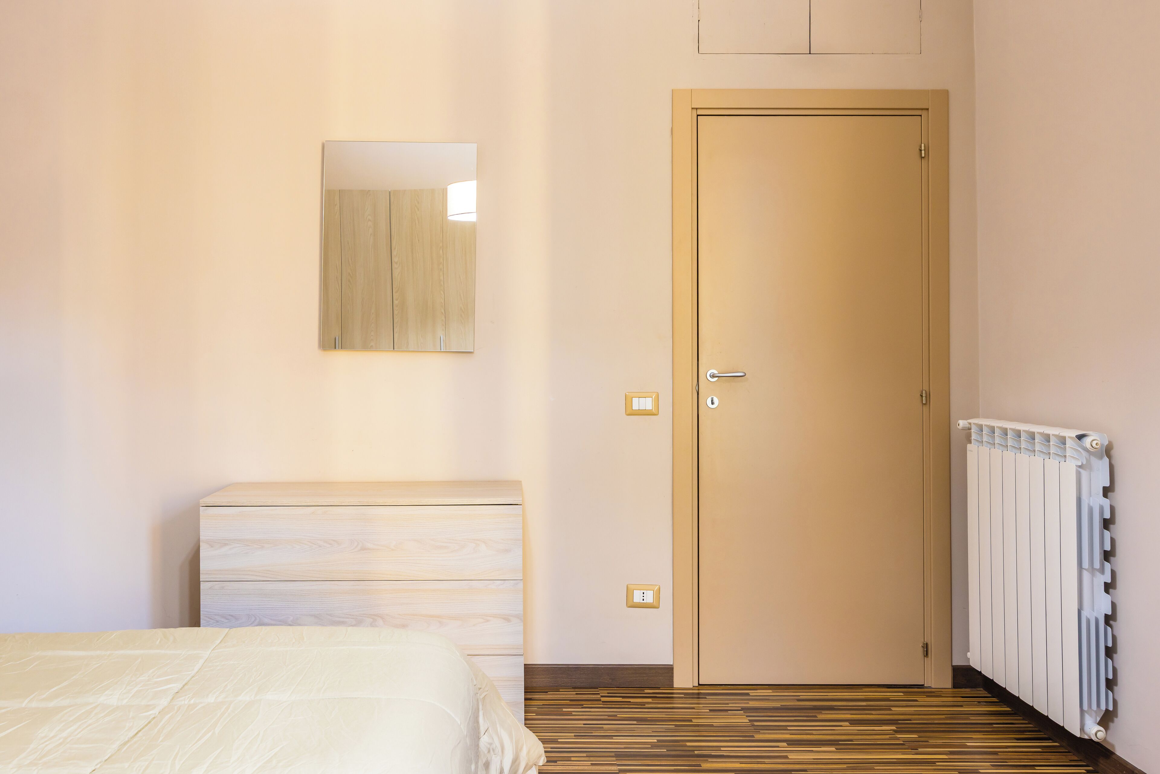 Een slaapkamer met een bed, een dressoir, een deur en een radiator.