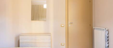 Een slaapkamer met een bed, een dressoir, een deur en een radiator.