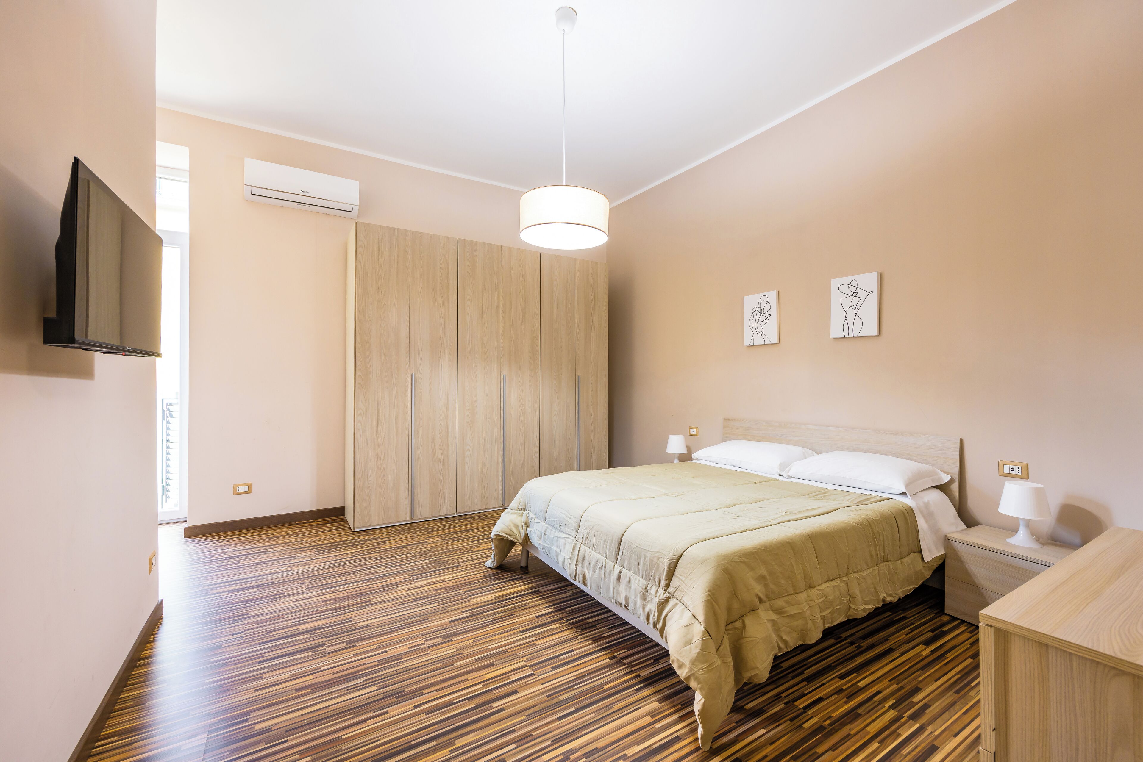 A bedroom with a bed, bedside tables, a TV, and artwork on the wall.