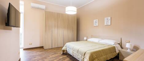 A bedroom with a bed, bedside tables, a TV, and artwork on the wall.