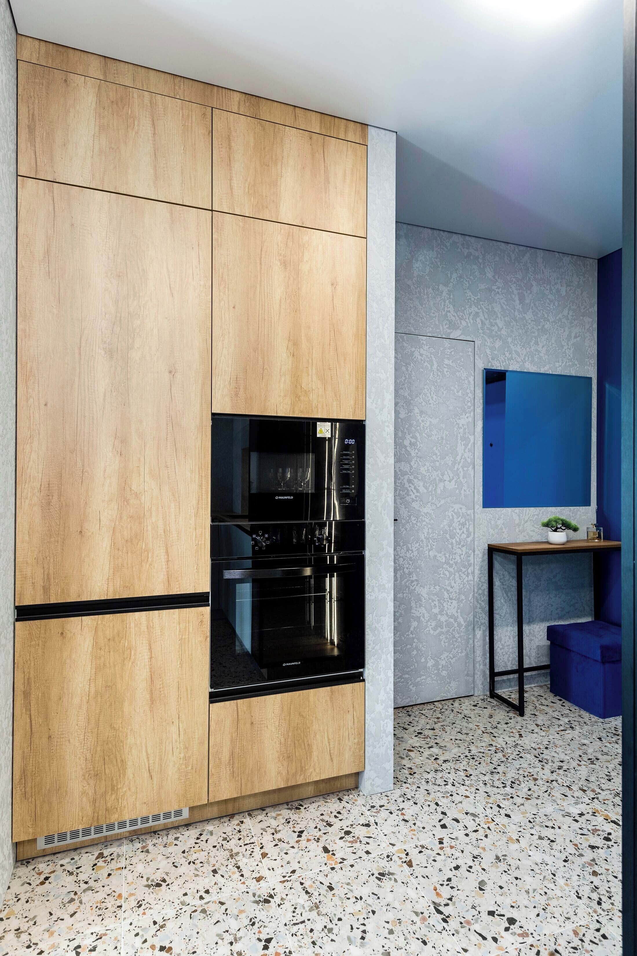 A kitchen with wooden cabinets, a black refrigerator, and a speckled floor.
