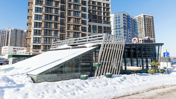 A modern building with a glass facade and a sloped roof, surrounded by snow. - Apartments near Aerodromnaya metro st (Minsk)