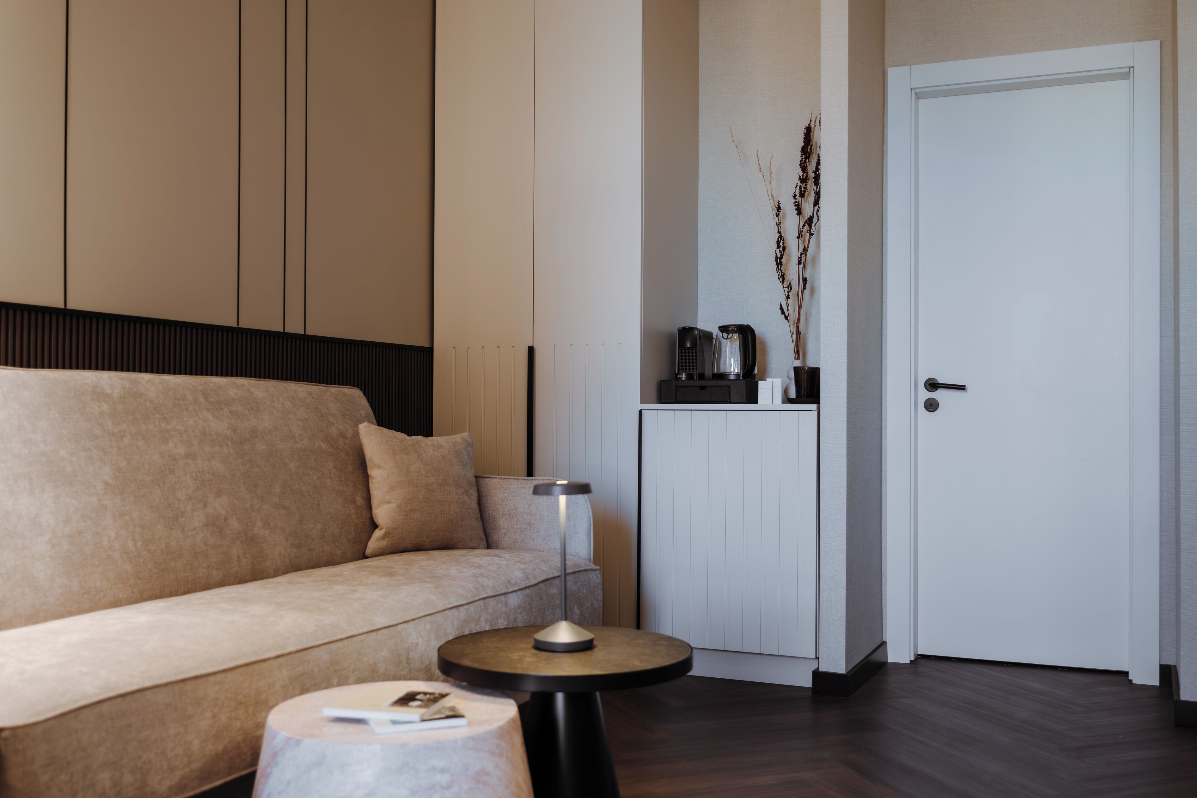 Ett modernt vardagsrum med en beige soffa, ett runt soffbord och ett vitt skåp med en vattenkokare.