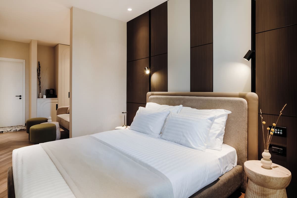 A modern bedroom with a large bed, a bedside table with a vase, and a wall-mounted control panel.