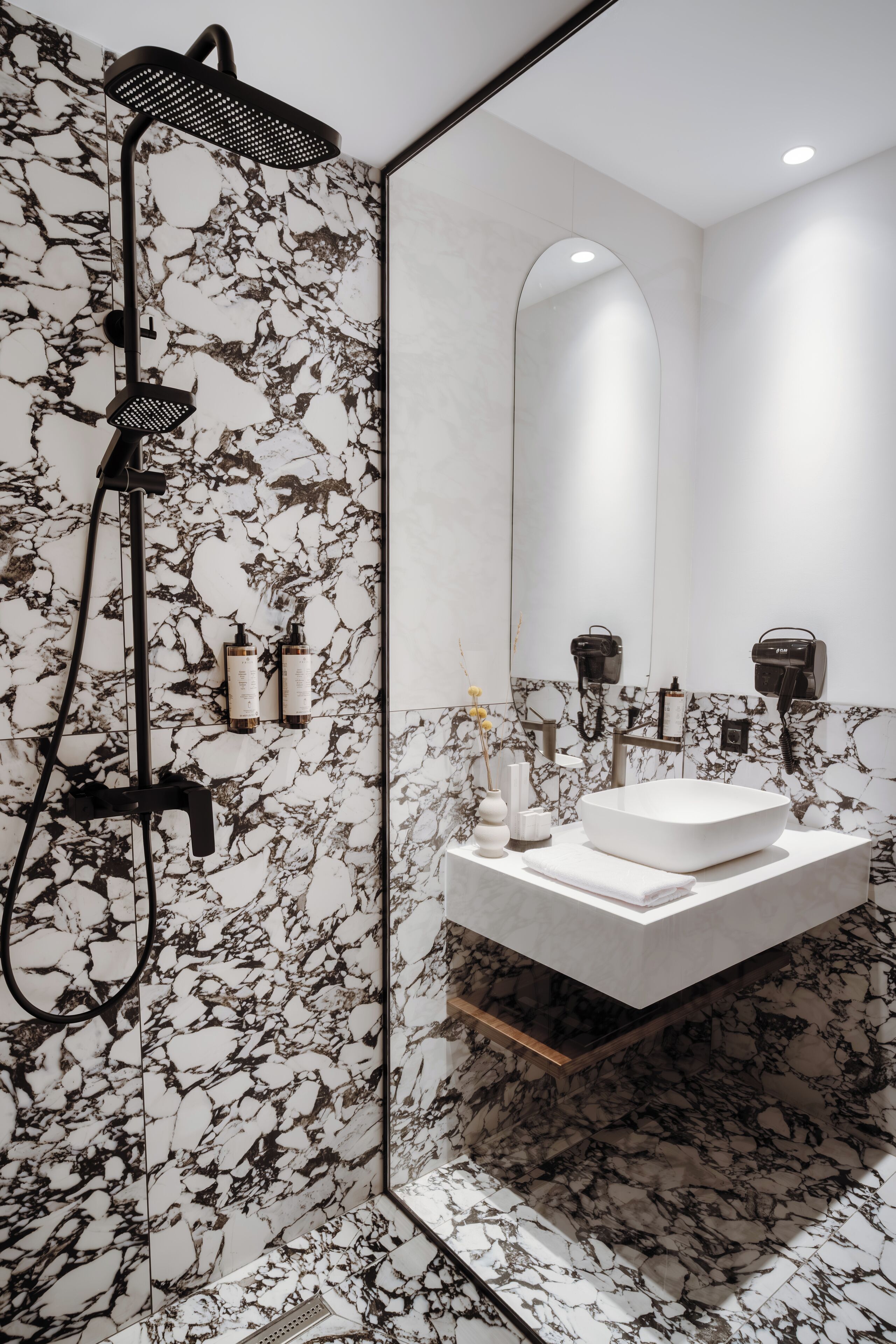 A modern bathroom with a large mirror, a white sink, and a black showerhead.