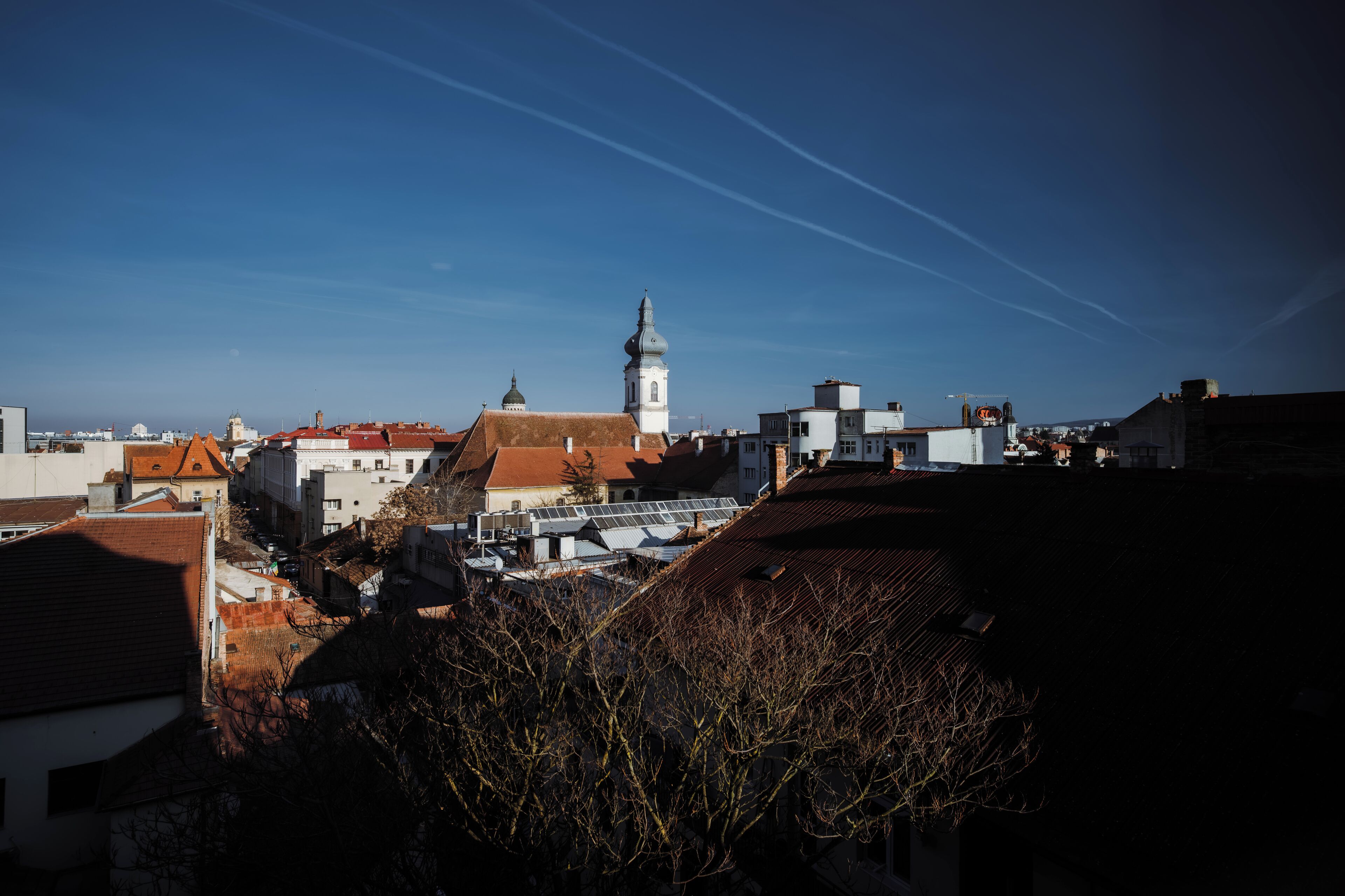 Paisagem urbana com uma torre de igreja imponente, diversos edifícios e céu claro.
