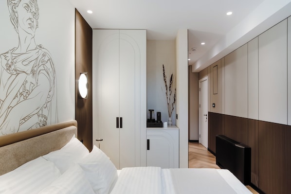 Un dormitorio moderno con una cama grande, un armario, un escritorio con un florero y un televisor.