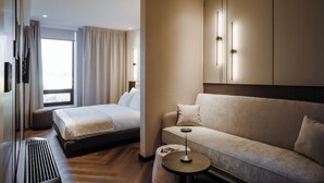 Ett modernt hotellrum med en säng, en soffa, ett litet runt bord och ett stort fönster.