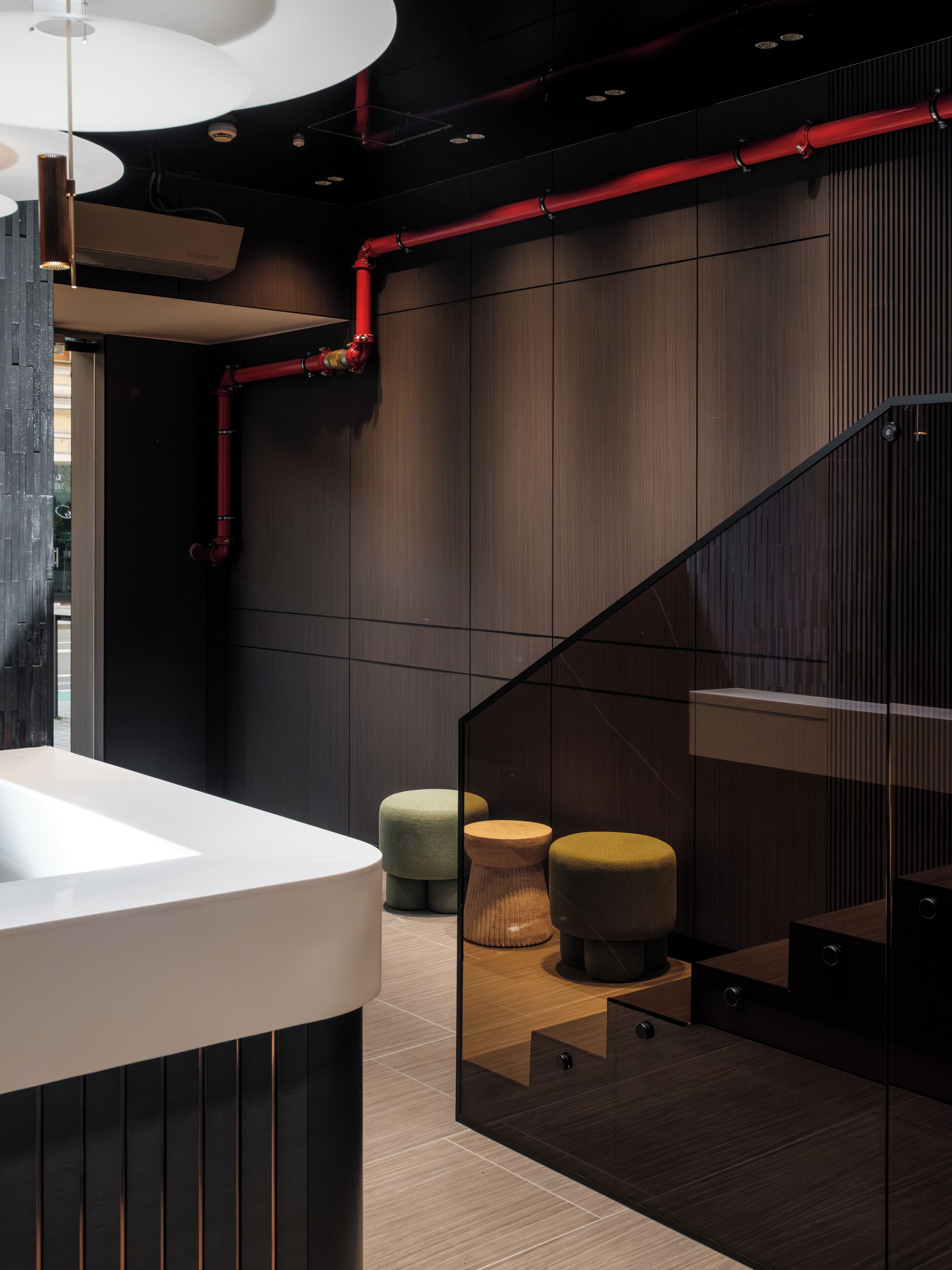 A modern interior with a white sink, wooden panel walls, red pipes, and a glass staircase.
