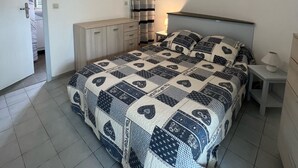 Ein Schlafzimmer mit Bett, Deckenventilator, Nachttisch, Lampe, Kleiderschrank und einem durchgegangenen Tür sichtbar erkennbaren Badezimmer.