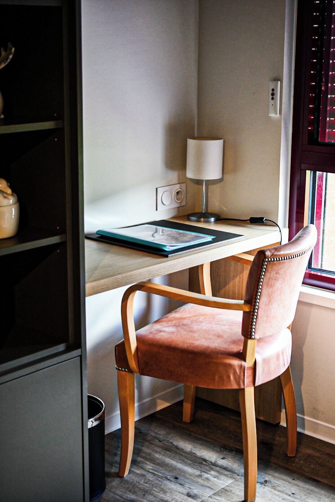 A desk with a lamp, a chair, and a window with blinds.