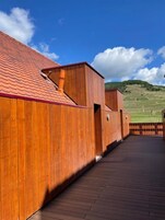 Um edifício de madeira com telhado vermelho, um deck de madeira e vista para colinas verdes ao fundo.