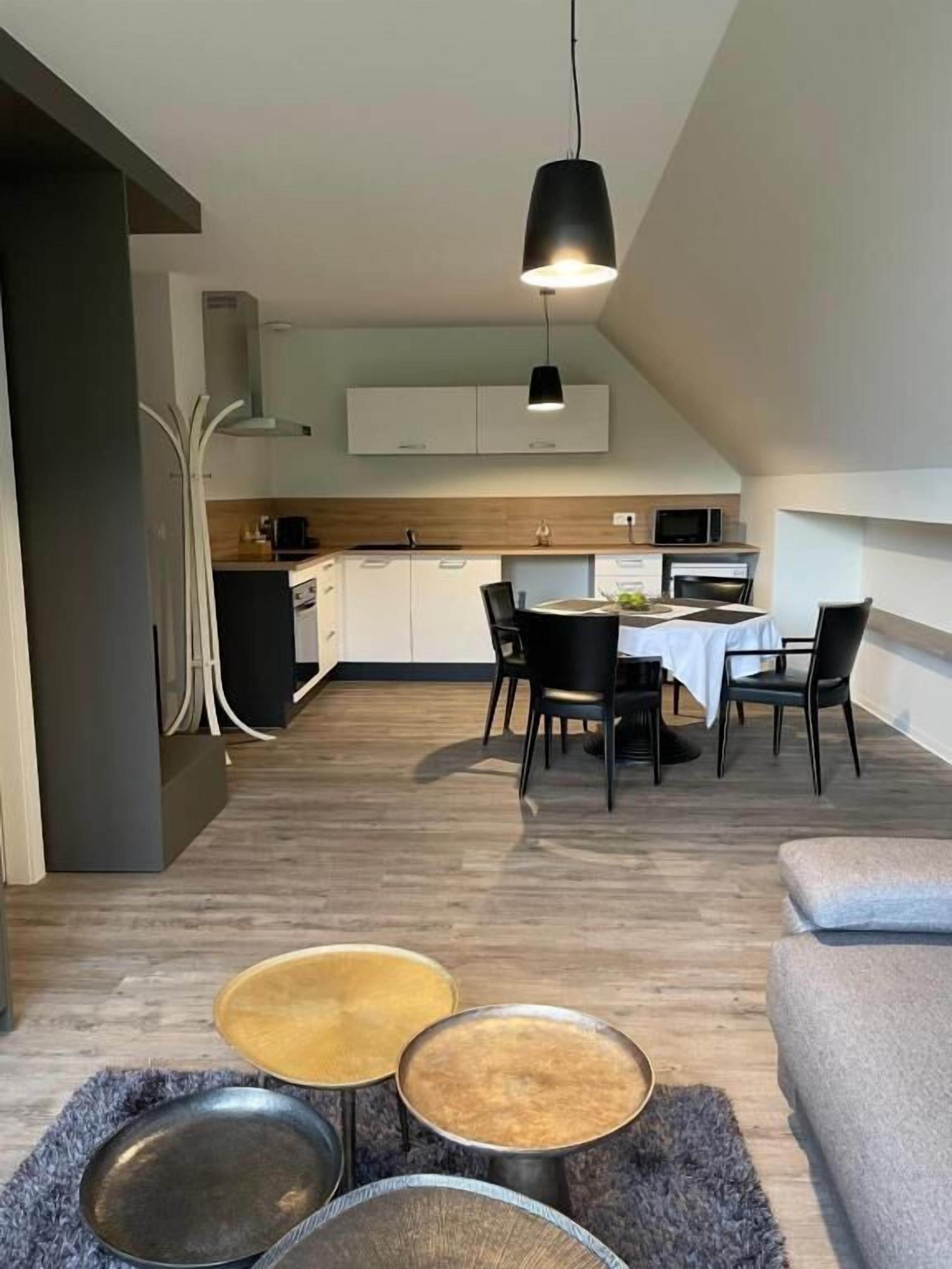 Una cocina moderna con armarios blancos, un comedor con mesa y sillas, y un sofá gris.