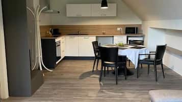 Una cocina moderna con armarios blancos, un comedor con mesa y sillas, y un sofá gris.