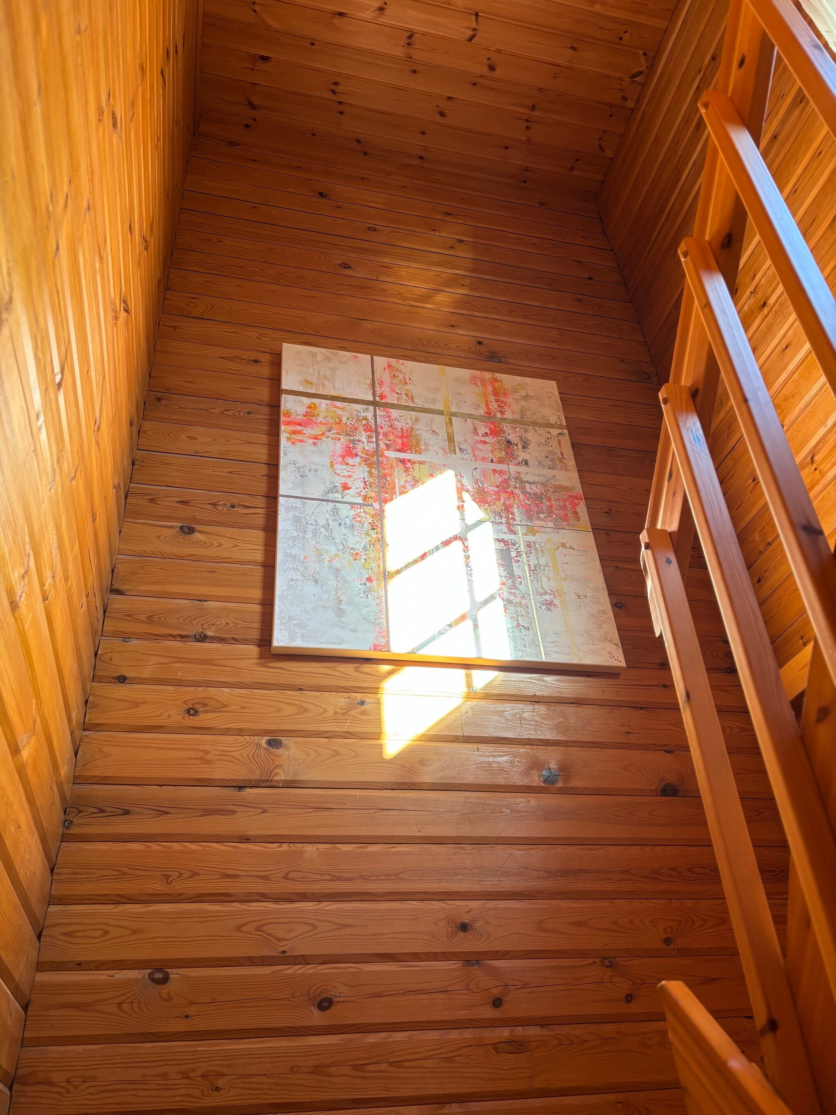 A wooden interior with a sloped ceiling, a wooden ladder, and a wall with a window.
