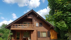 A two-story wooden house with a balcony, a front porch, and a well-maintained lawn.