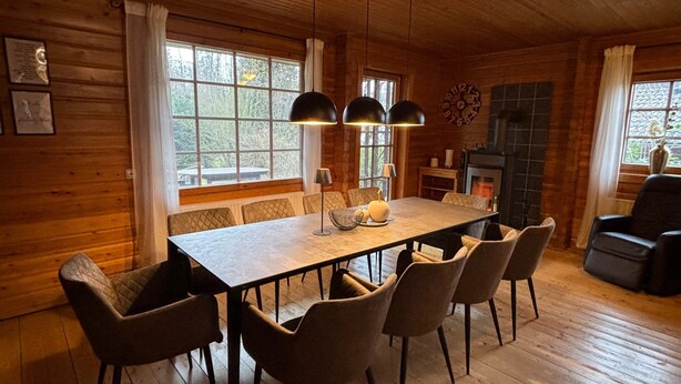 A wooden interior with a dining table, chairs, pendant lights, and a fireplace.