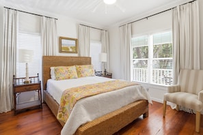 Un dormitorio con una cama grande, una mesita de noche, una silla y una ventana con persianas.