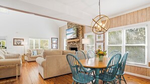 A spacious living room with a wooden floor, beige sofas, a dining table with blue chairs, and a stone fireplace. - 0.2 Mi to Beach • 3 Ensuite Baths • Sleeps 10 • Walk to King & Prince (St Simons)