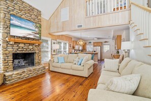 A spacious living area with a stone fireplace, wooden flooring, and a large couch. - 0.2 Mi to Beach • 3 Ensuite Baths • Sleeps 10 • Walk to King & Prince (St Simons)