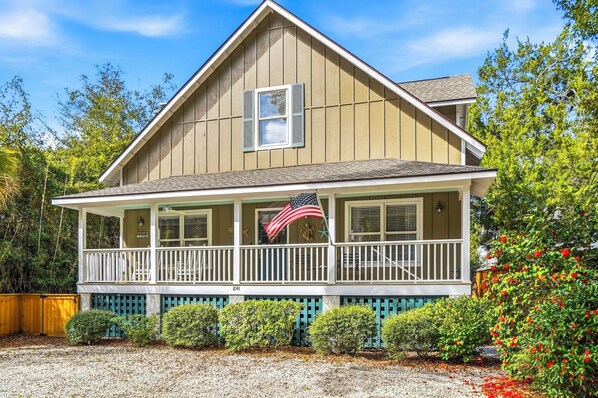 A two-story house with a porch, a small American flag, and a mailbox. - 0.2 Mi to Beach • 3 Ensuite Baths • Sleeps 10 • Walk to King & Prince (St Simons)