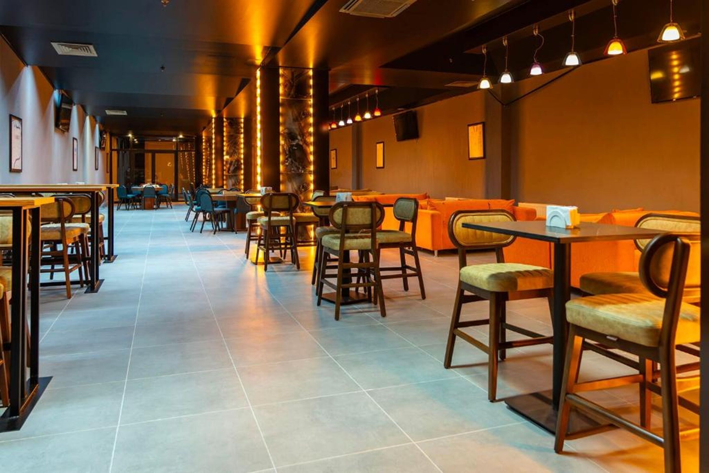 Un restaurante con una barra larga, mesas en cabinas y mesas altas.