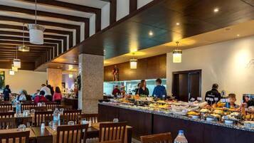 A buffet area with multiple food stations, wooden tables and chairs, and a kitchen in the background.