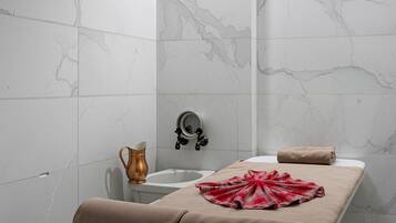 Un cuarto de spa con una camilla de masaje, una jarra color cobre y una toalla.