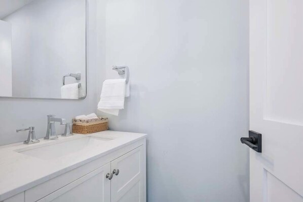 A modern bathroom with a white vanity, two sinks, a large mirror, and a basket of toiletries. - 5 bedroom Close to beaches, island ferries and Main St Hyannis RPMS164 (Hyannis)