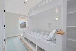 Ein Etagenbett mit Holz-Kopfstück, ein Nachttisch und ein Fenster mit Blick auf Bäume.