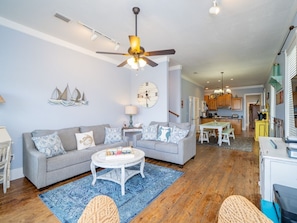 A living room with a sofa, coffee table, and a ceiling fan. There is a kitchen area visible in the background. - Family Friendly/Lagoon front w/Fishing Pier & Pool (Gulf Shores)