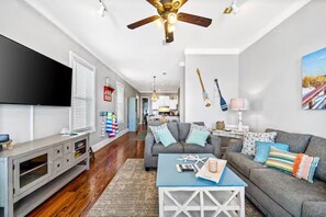 A modern living room with a grey sofa, a blue coffee table, and a ceiling fan. - Lagoon-front Duplex w/Fishing Pier Sleeps 24/BM (Gulf Shores)