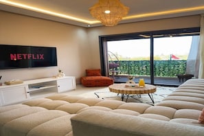 A modern living room with a large flat-screen TV, a sofa, a coffee table, and a balcony with a view. - New central 1BR /Balcony /AC - Walk to Majorelle (Marrakech)