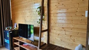 Habitación de cabaña de madera con literas, televisión, escritorio pequeño y estante con pantuflas.